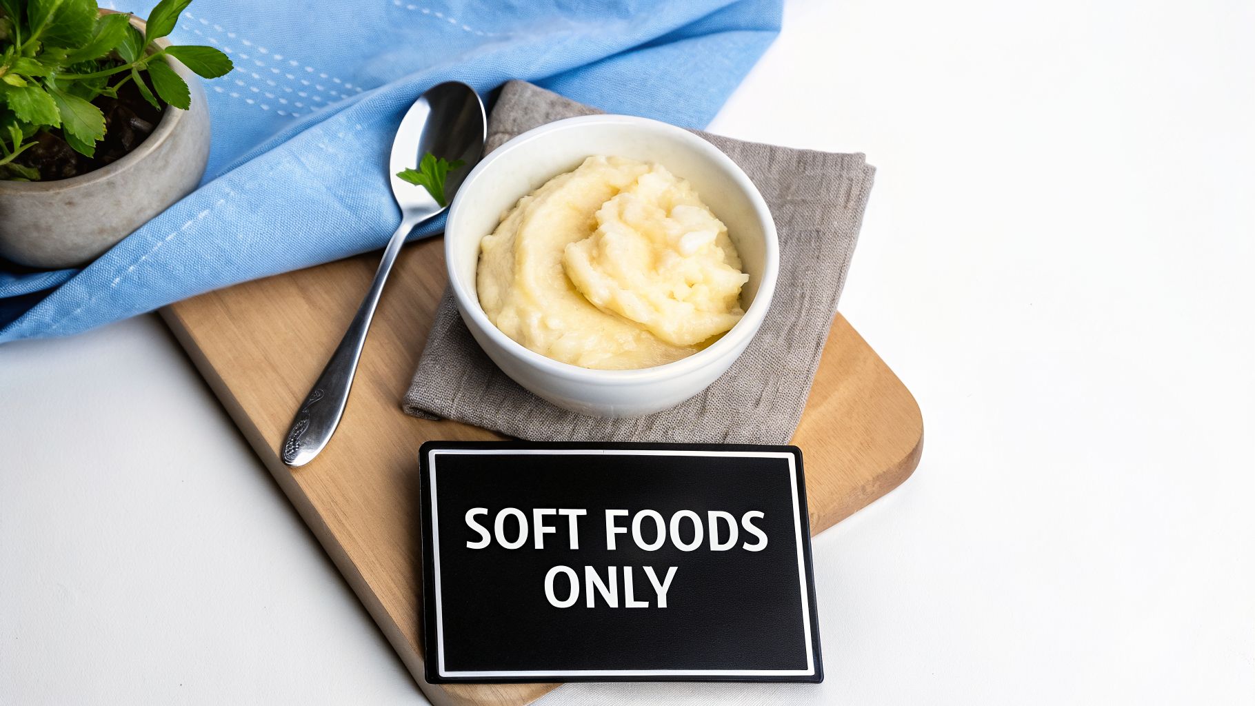 A bowl of soft mashed potatoes with a spoon, a plant, and a 'SOFT FOODS ONLY' sign.