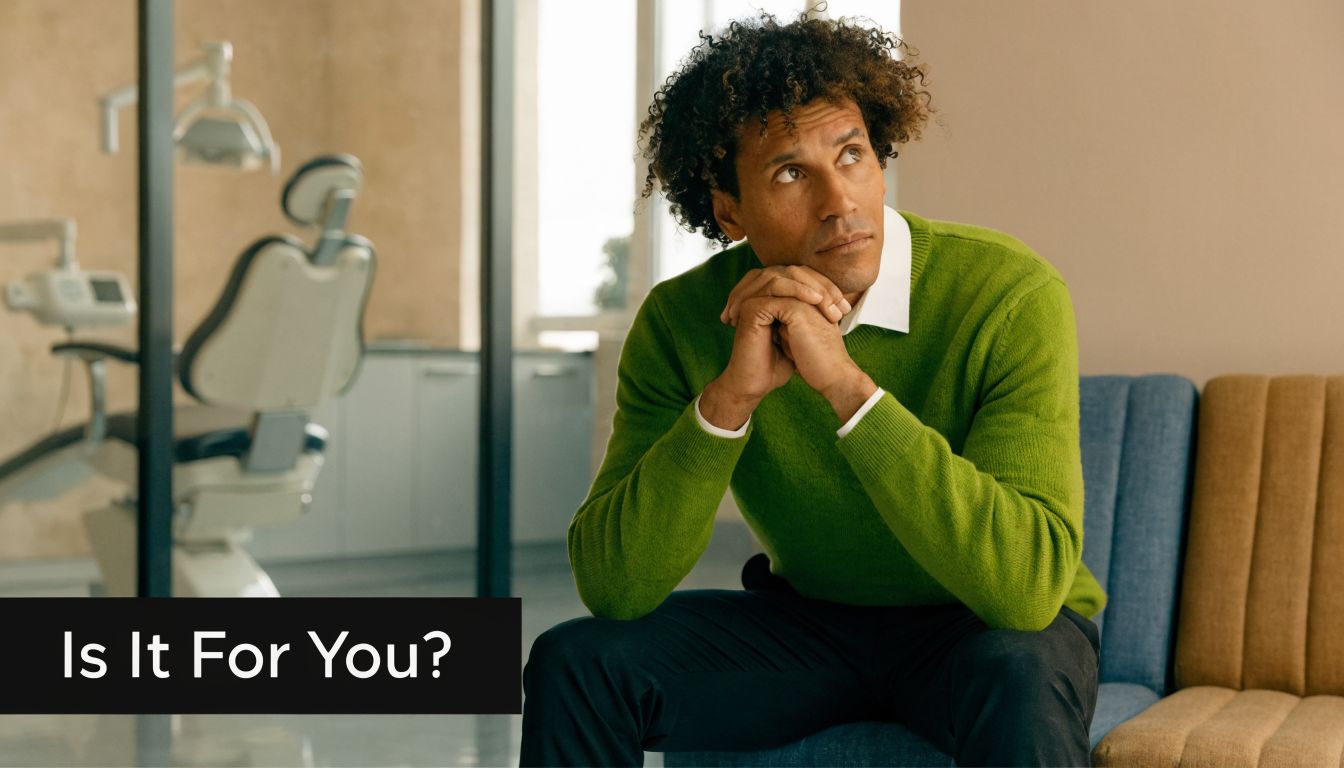 A man with curly hair wearing a green sweater looking thoughtful while sitting in a dental office.
